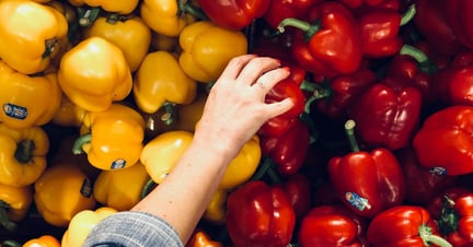 A hand picking vegetable from a wall of colourful red and yellow peppers